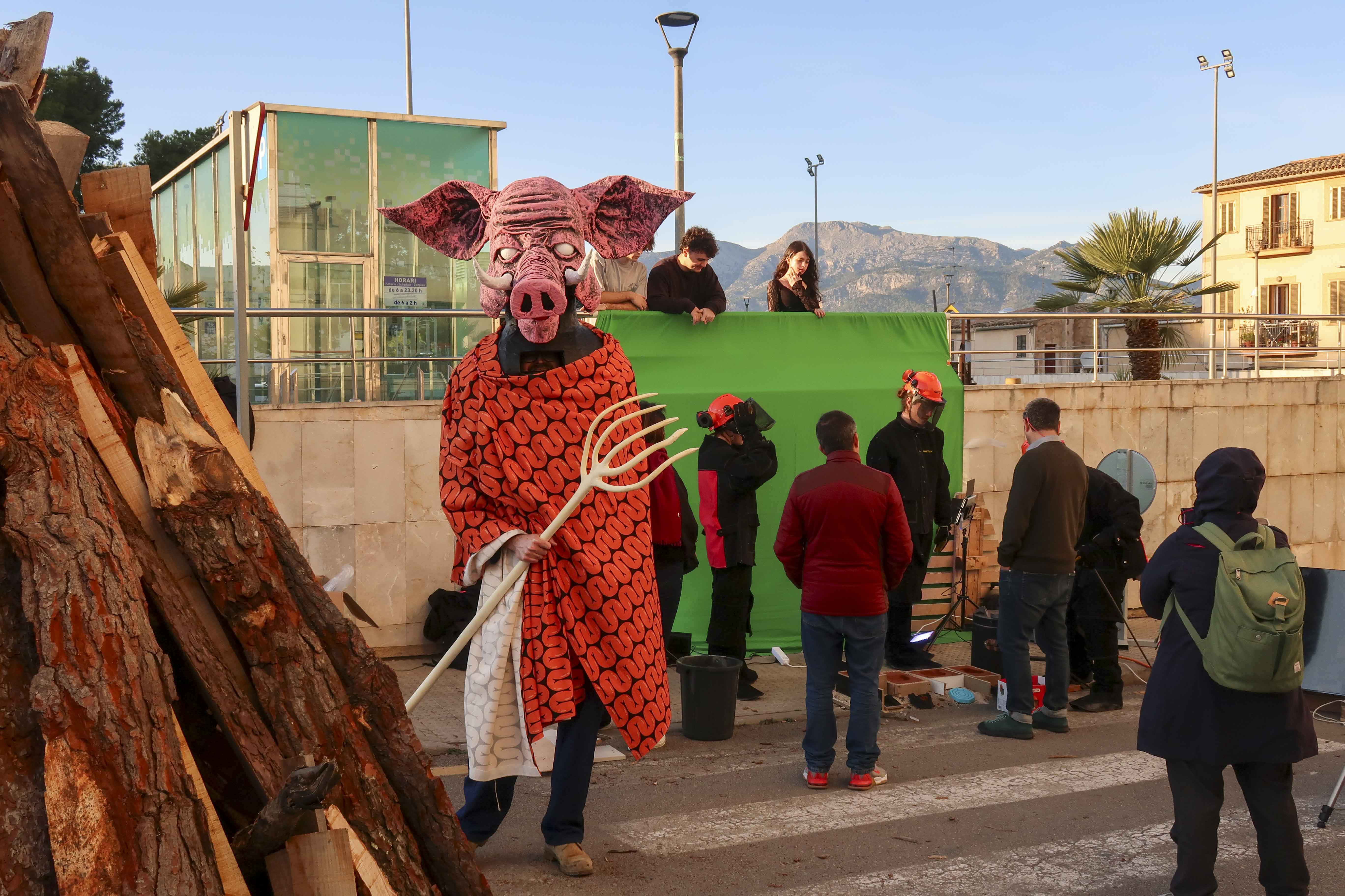 A man in a pig costume standing next to students, a green screen, and a stack of wood